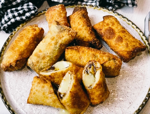 Crispy, golden spring rolls filled with brie and fig on a round white serving platter.
