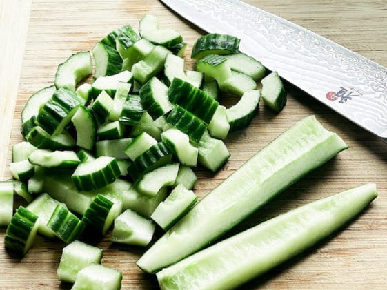 Chopped cucumbers on a wooden cutting board with a chef's knife along side.