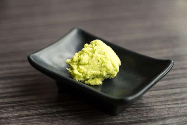A mound of wasabi paste on a small black platter on top of a wooden surface.