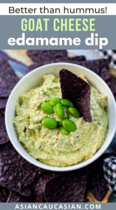 Goat cheese edamame dip in a small white bowl with edamame pods and blue corn tortilla chips on the side.