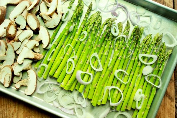 Fresh asparagus and shiitake mushrooms on a tray with shallot rings on top