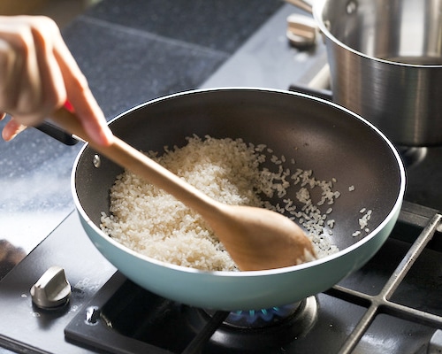 A woman frying rice in a blue wok on top of the stove.