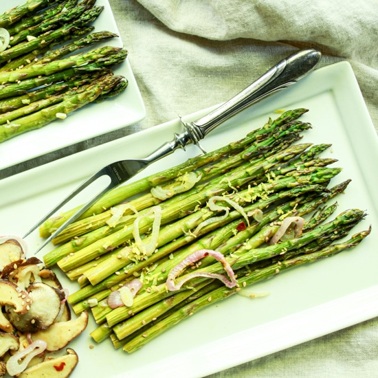 Roasted asparagus and shiitake mushrooms on two white trays with a serving fork on the side.