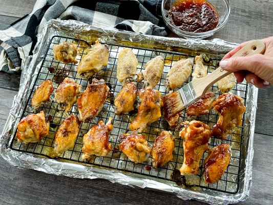 Pieces of chicken wings placed on a wire rack being brushed with wing sauce.
