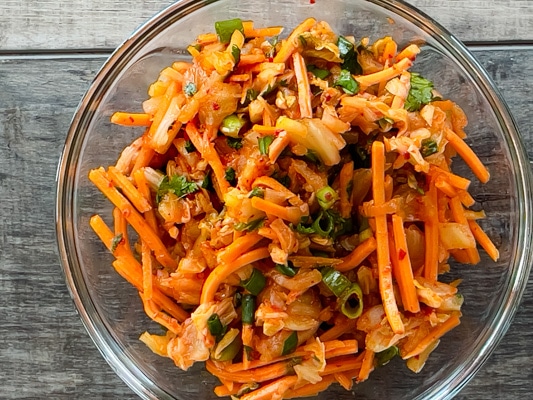 Kimchi slaw in a clear glass bowl on top of a gray wooden board.