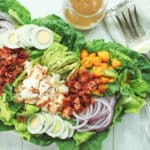 A platter of vibrant lobster cobb salad on top of romaine greens and a clear jar of miso dressing on the side.