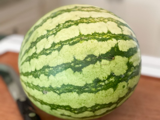 A whole round watermelon on top of a wooden board.