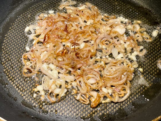 Caramelized onions being cooked in a black frying pan.