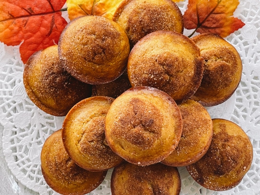 A stack of pumpkin muffins on a white doily with fall leaves.