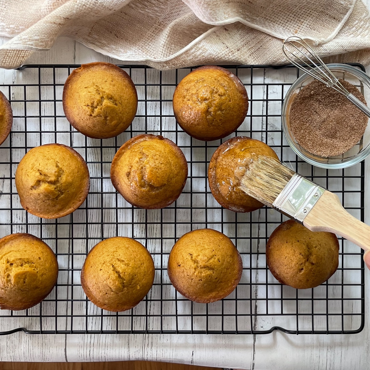 Classic pumpkin muffins on a baking rack being brushed on top with melted butter.