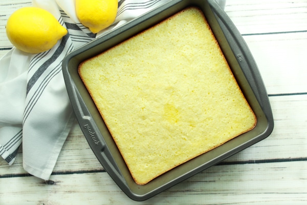 A gray baking tray filled with baked lemongrass coconut bars on a white board with fresh lemons on the side.