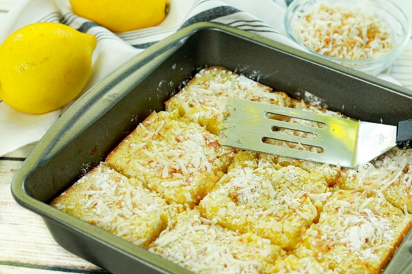 A gray baking tray filled with baked lemongrass coconut bars cut into squares with a spatula on top.