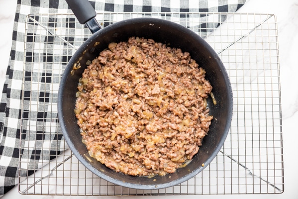 Ground pork and onions cooked in a frying pan on top of a wire rack.