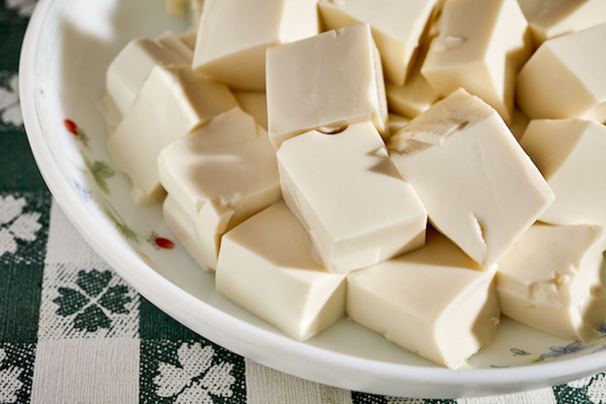 Cubes of silken tofu in a white bowl on top of a checkered napkin.
