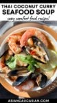 A white bowl of Thai seafood soup with shrimp, mussels and lime on top of a rust-colored plate placed on a wooden board.