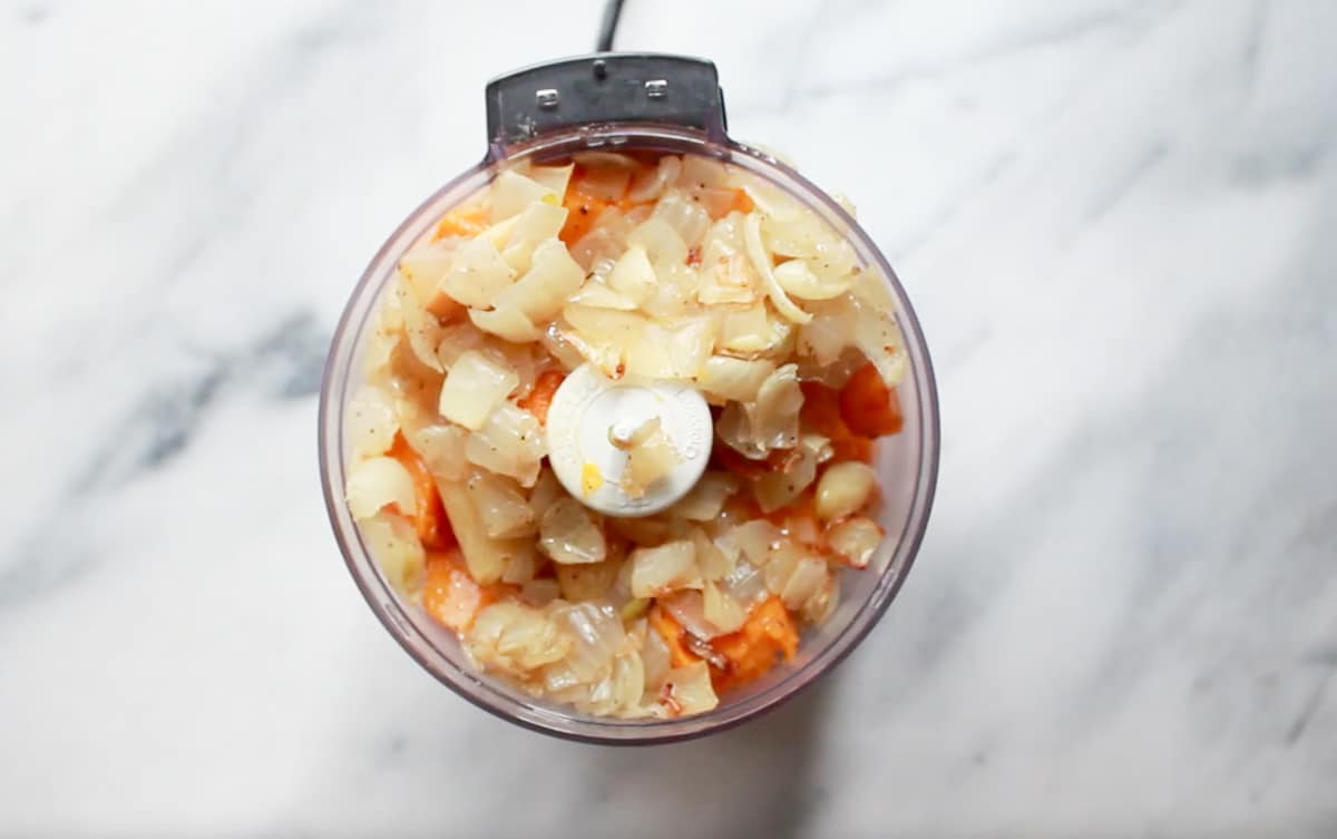 Roasted chopped onions and butternut squash in a mini food processor on top of a marble surface