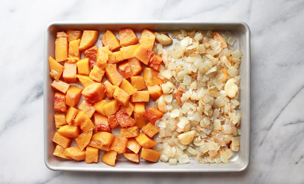 Roasted cubed butternut squash, chopped onions, and garlic cloves on a baking tray.