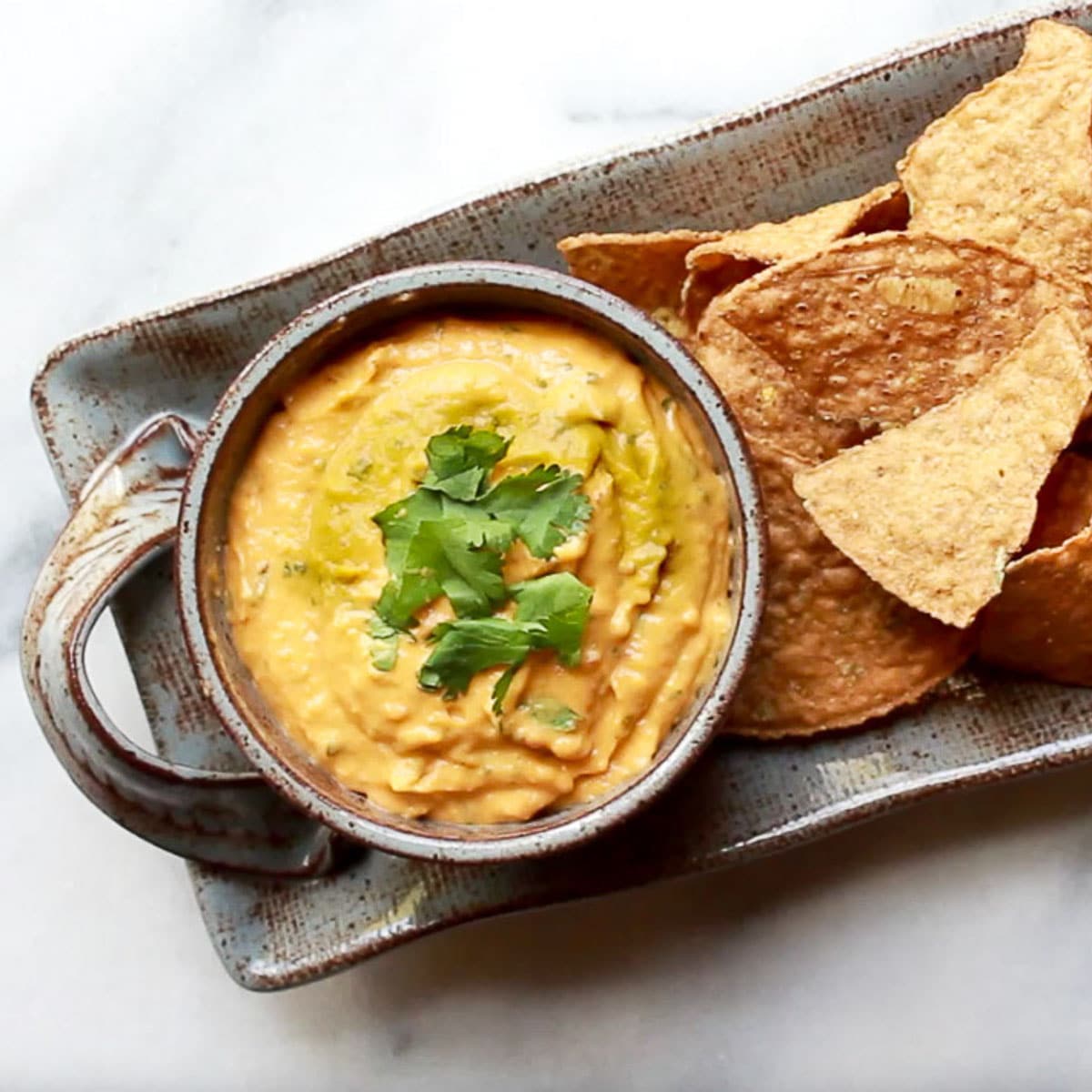 roasted thai butternut squash dip in a gray bowl on top of a gray serving platter with tortilla chips on the side on top of a marble surface