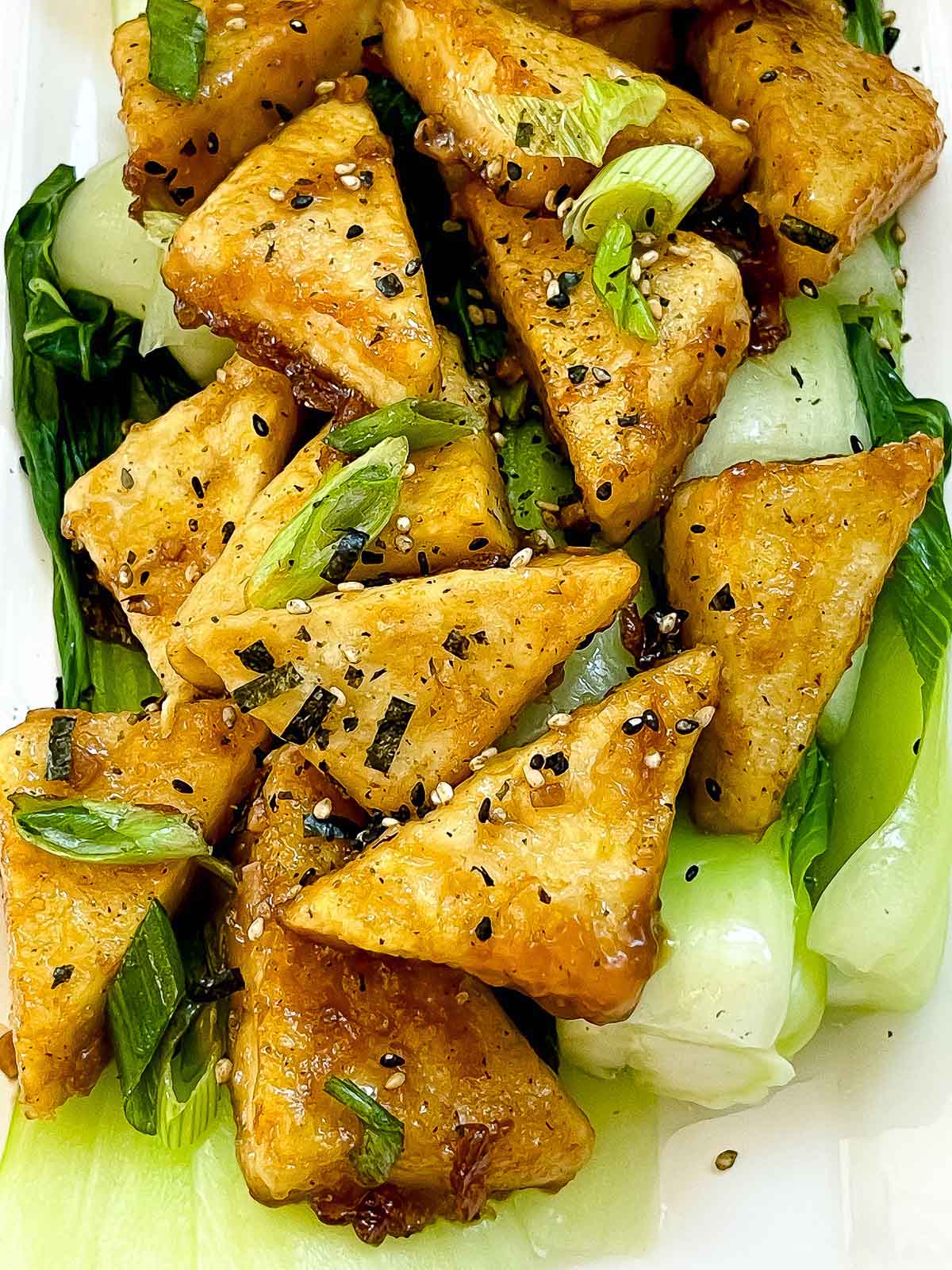 Golden-brown, crispy tofu steaks piled on top of cooked baby bok choy and sprinkled with seasonings.