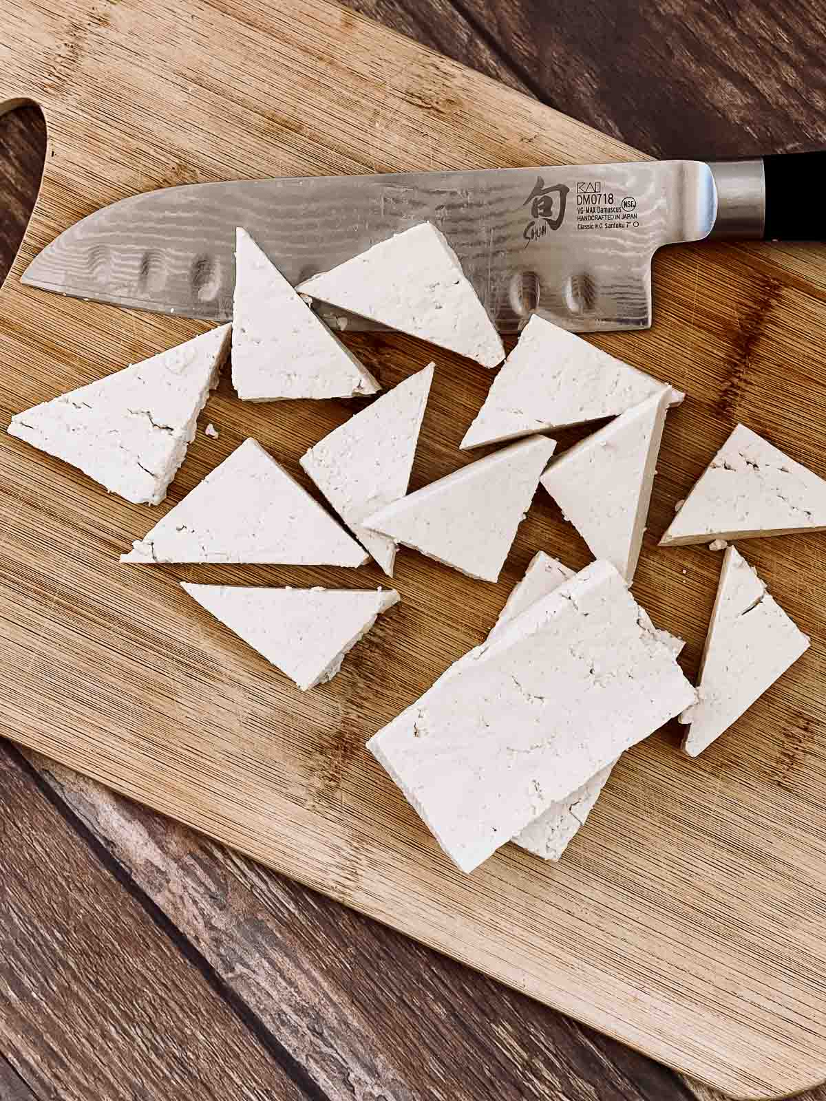 Cut tofu triangles on a wooden cutting board with a chef's knife on the side.