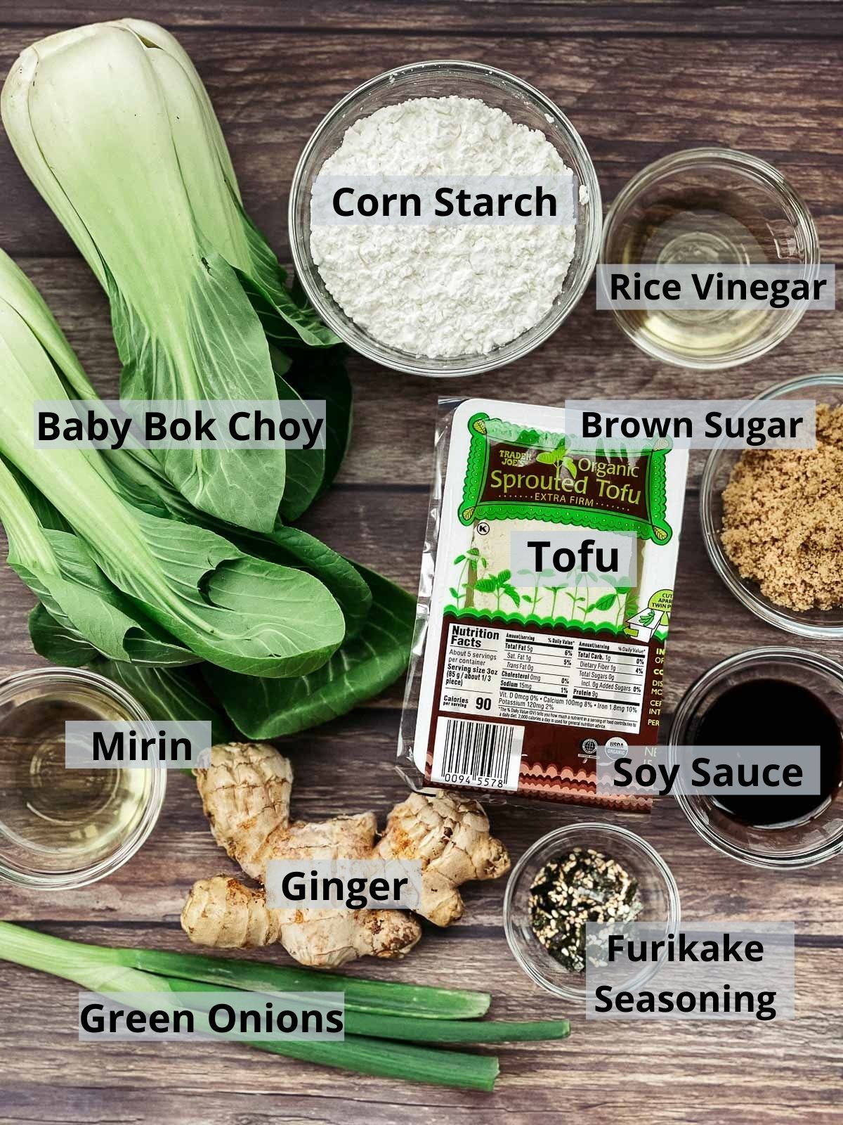 Labeled ingredients for making crispy tofu with bok choy on top of a wooden board.