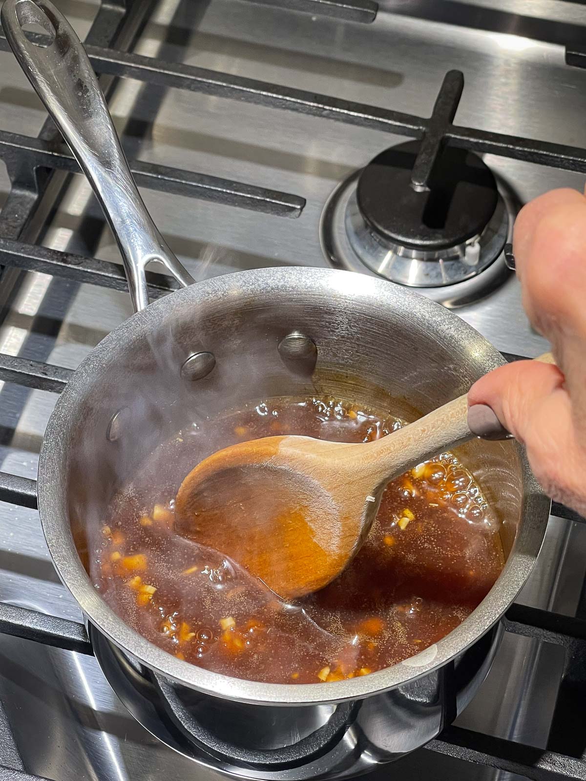 An Asian sauce being stirred in a sauce pot with a wooden spoon on top of a stove.