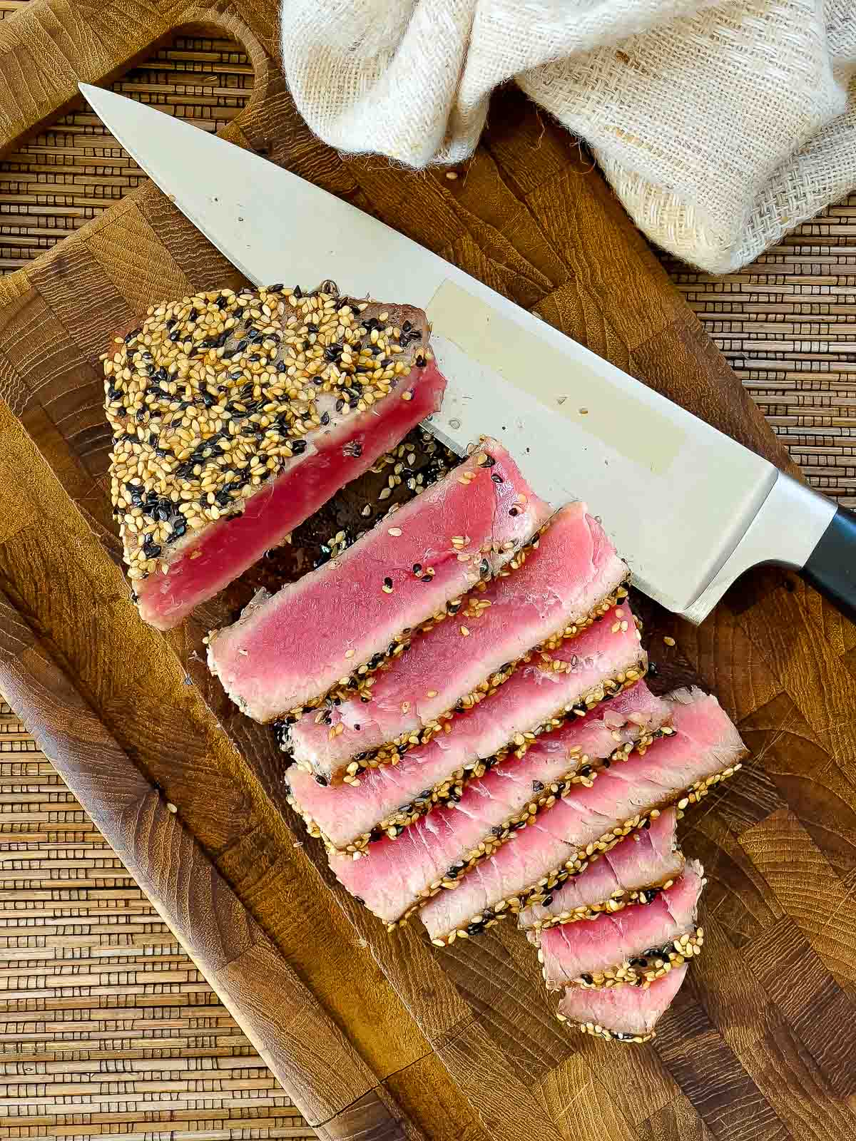 Beautifully seared tuna steak sliced on a wooden cutting board with a chef's knife on the side.
