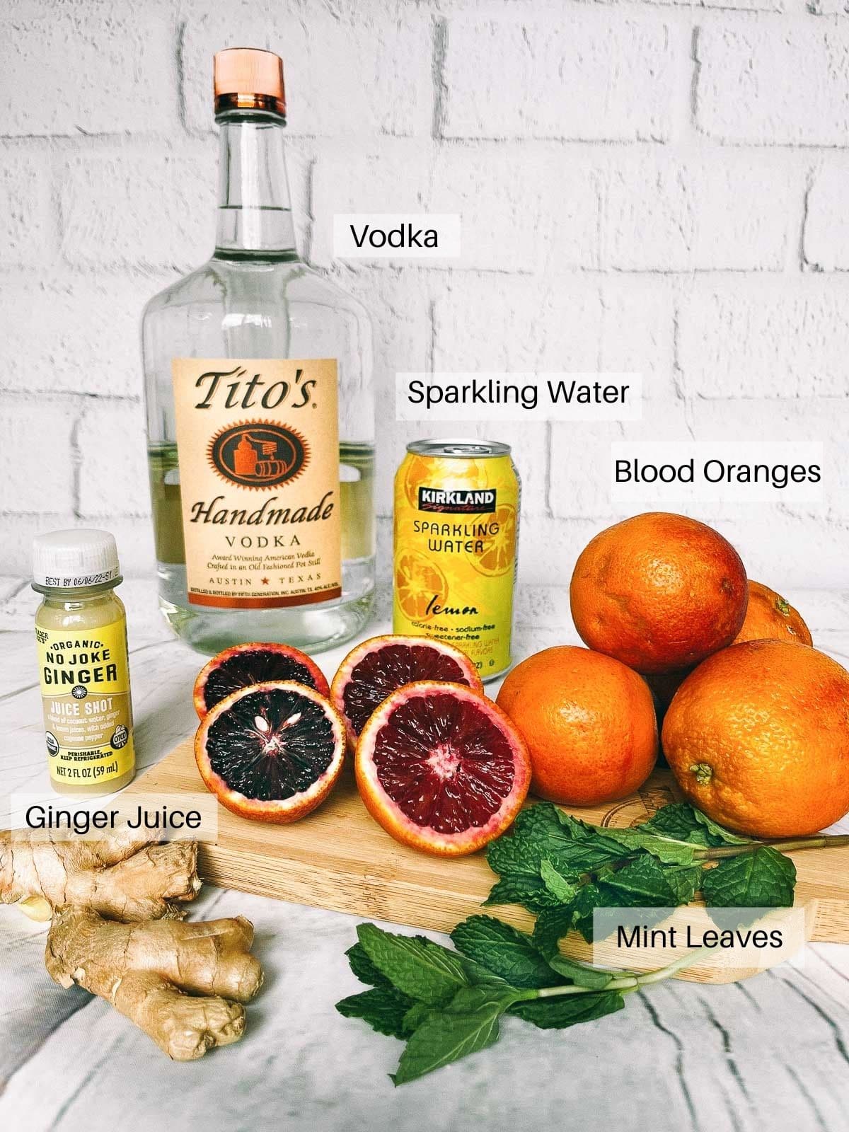 Labeled ingredients for making a blood orange ginger cocktail on top of a white board