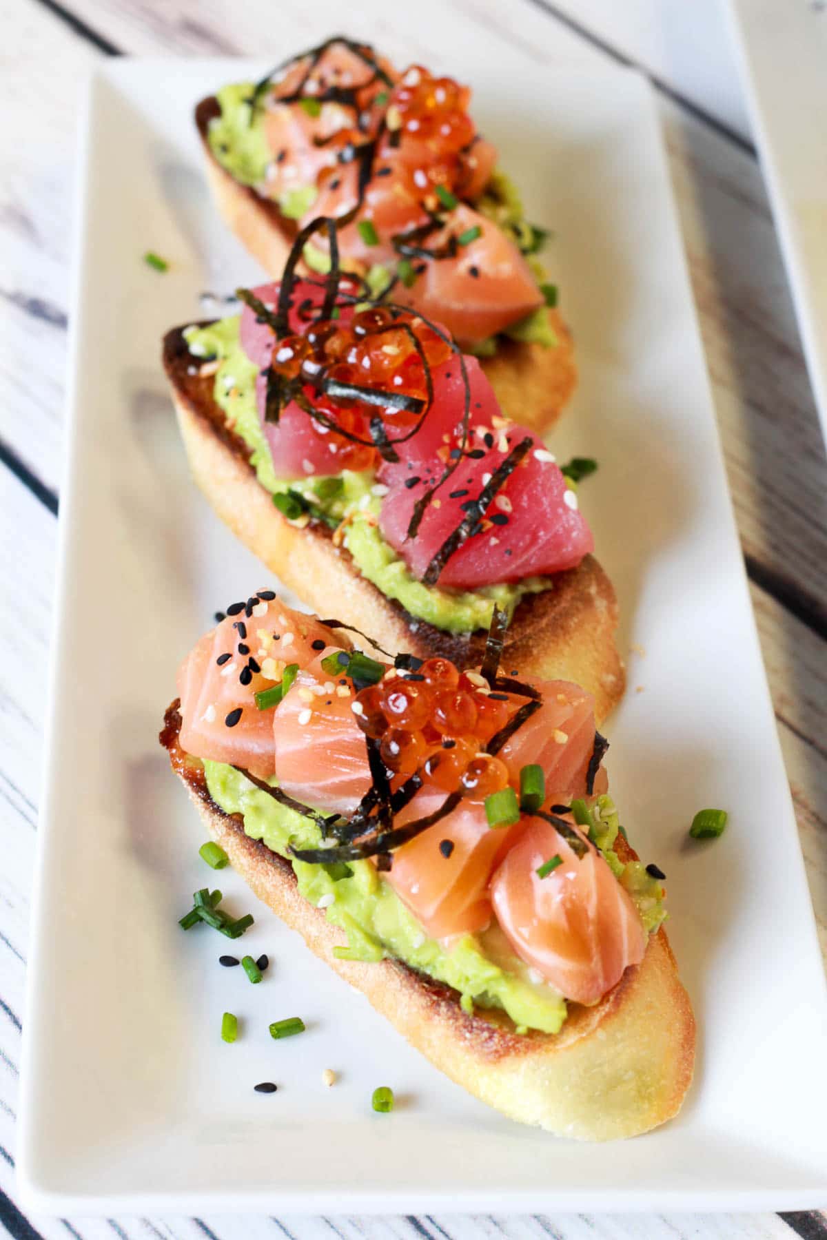 sushi grade tuna and salmon on avocado toast placed on a white platter