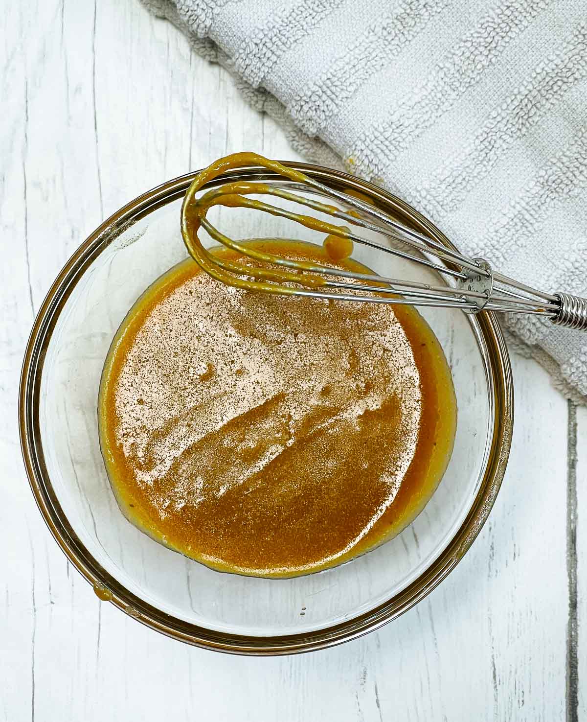 Miso marinade sauce in a clear bowl with a small whisk on top of a white wooden board.