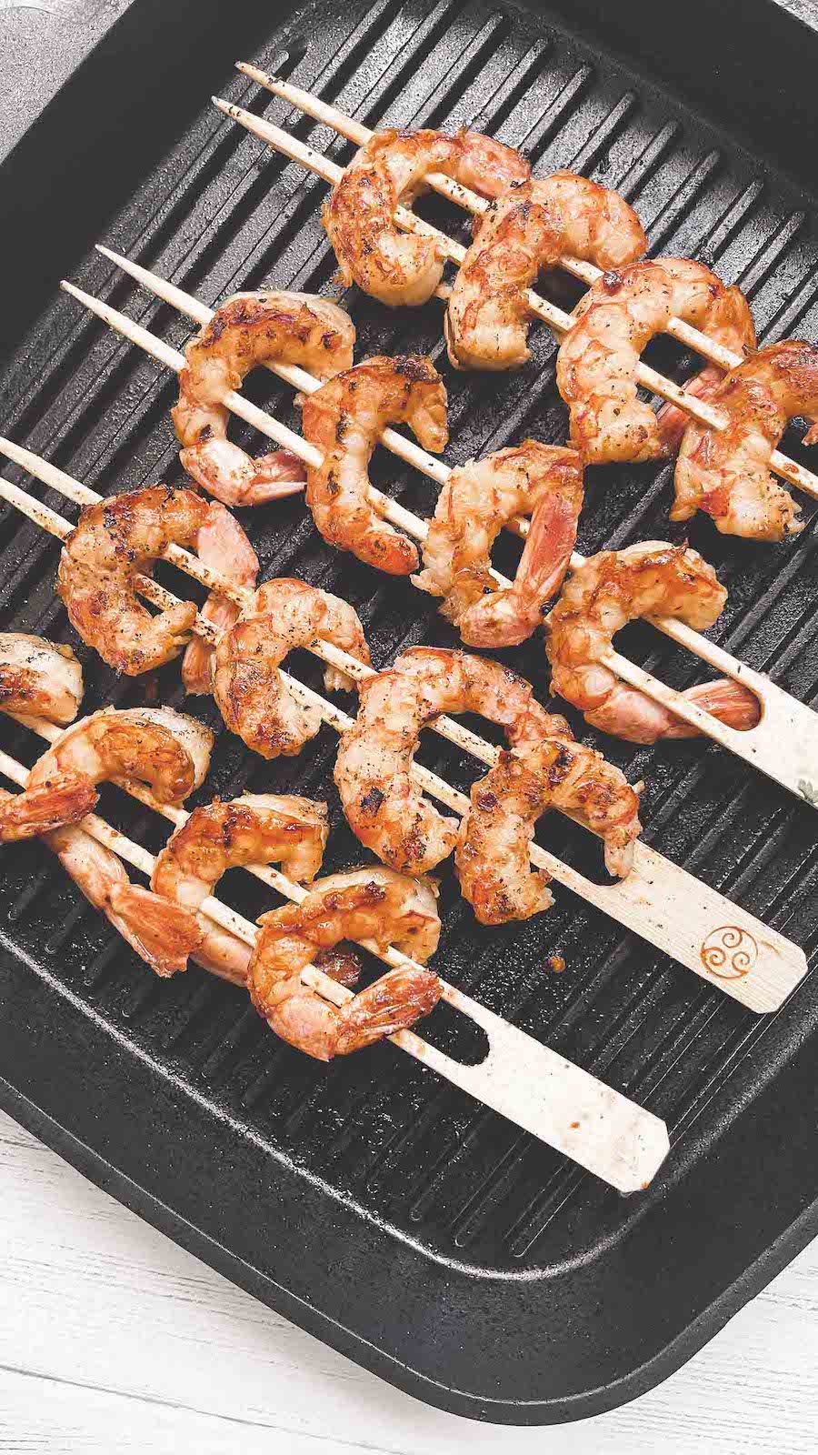 Shrimp of wooden skewers grilling on a black grill pan.