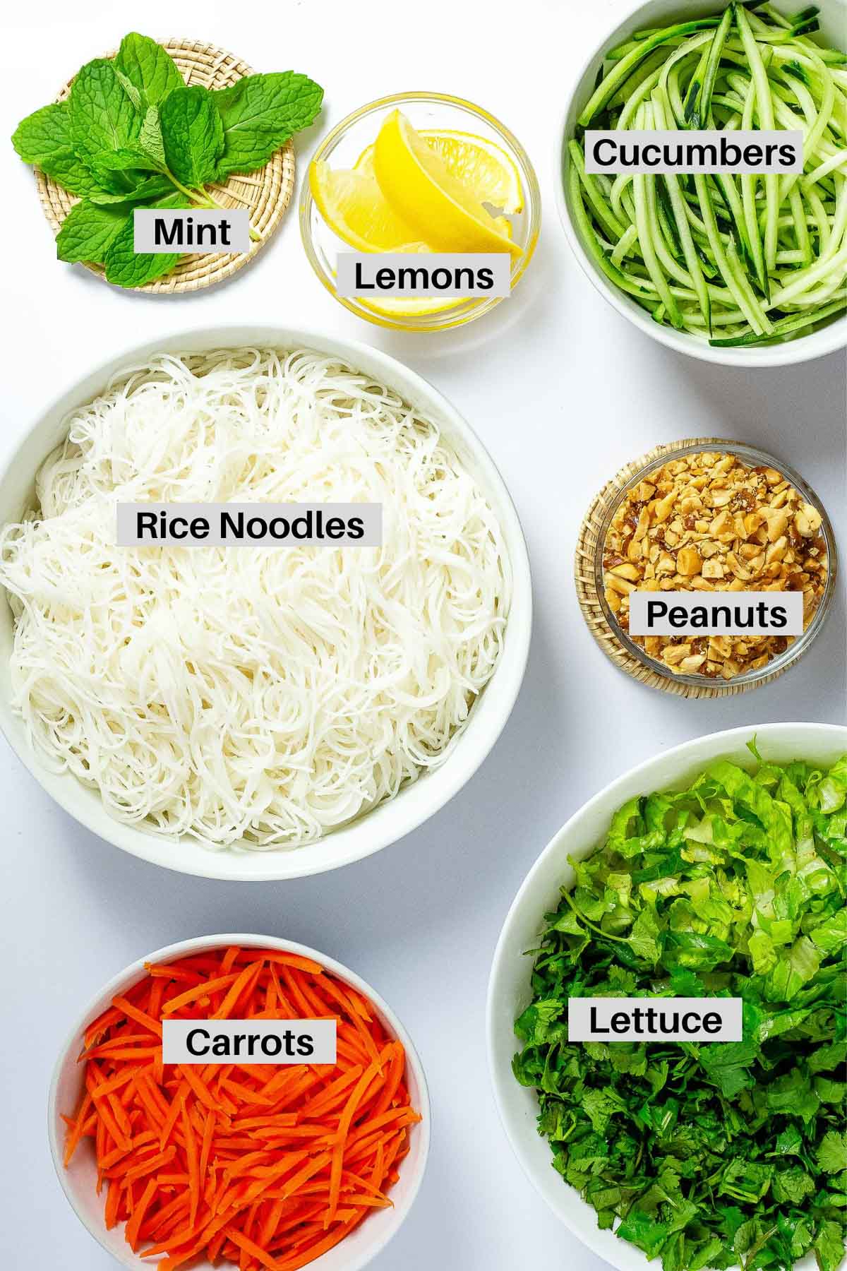 Labeled ingredients in bowls for making Asian beef noodle bowls on top of a white surface.