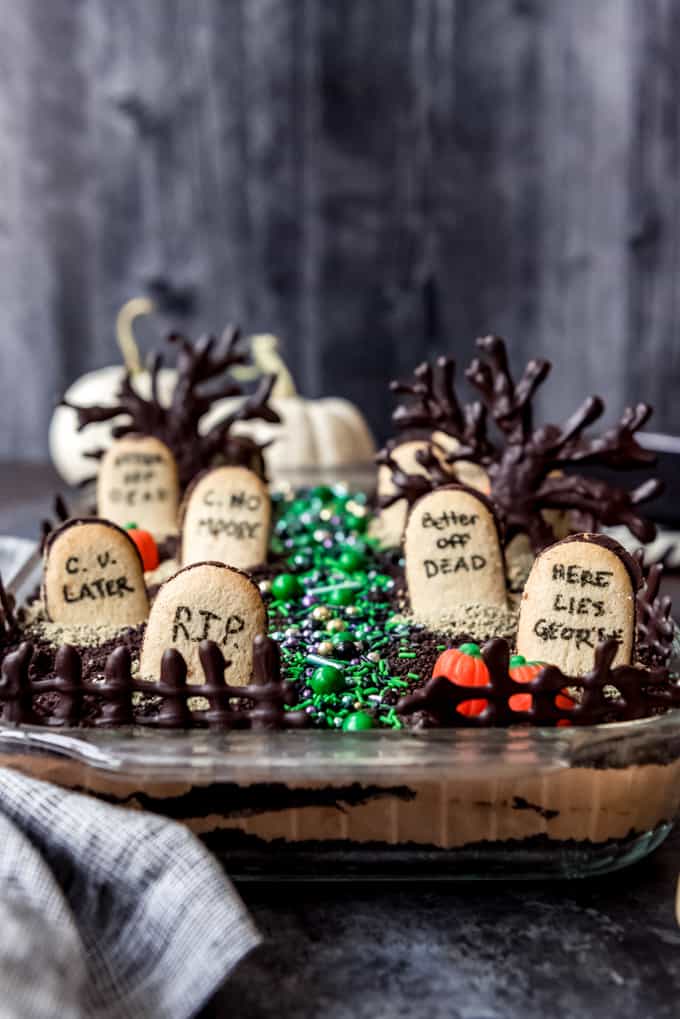 graveyard dirt cake with scary tombstone Halloween cookies on top of chocolate pudding in a glass pie plate with chocolate trees in the background