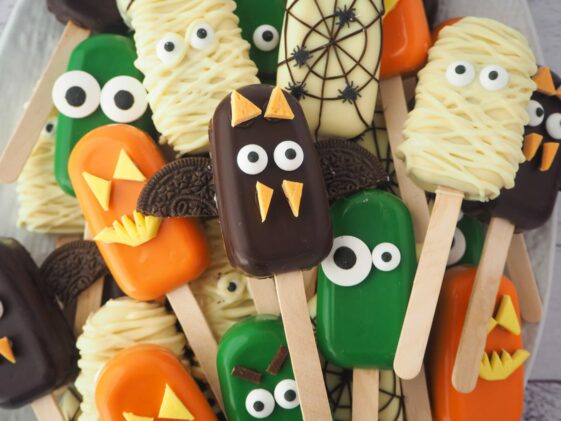 colorful, decorated Halloween cakesicles on a stick piled on top of each other with funny monster faces