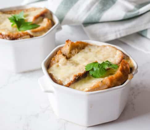 Instant Pot French Onion Soup in two white bowls topped with melty cheese bread on a white surface