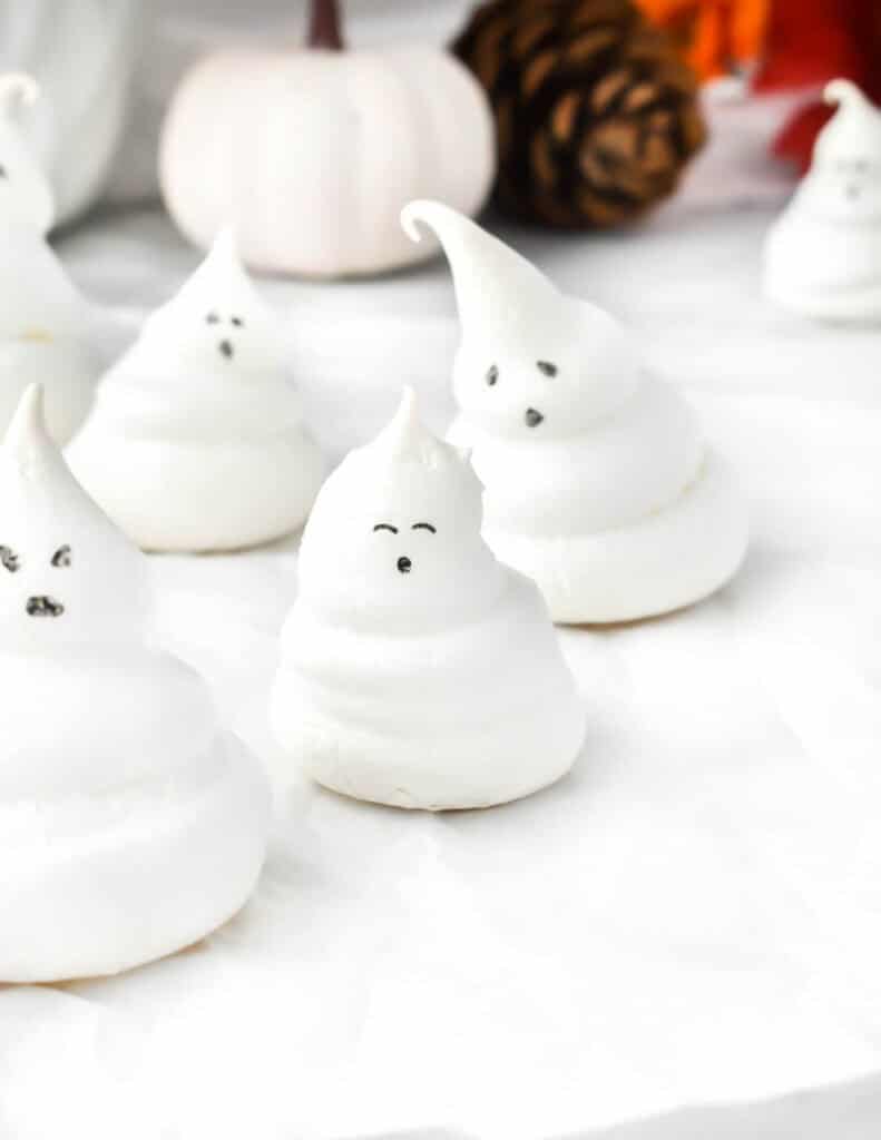 meringue ghosts with eyes and mouths on top of a white surface for Halloween