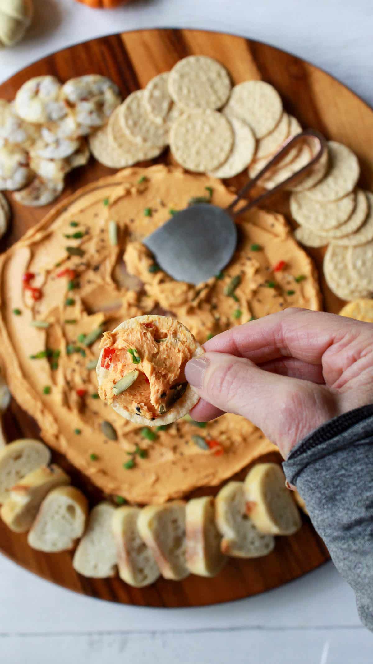 a hand holding up a cracker with miso butter over a round miso butter board surrounded by crackers and bread