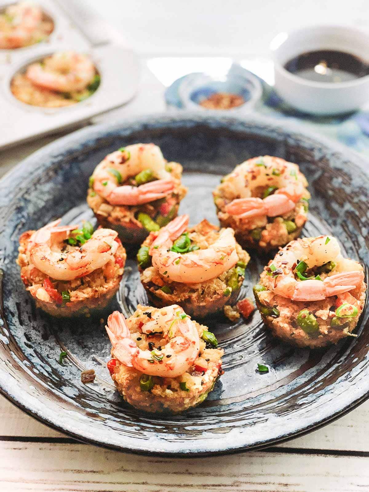 fried rice cups topped with shrimp on a round plate on top of a white wooden board