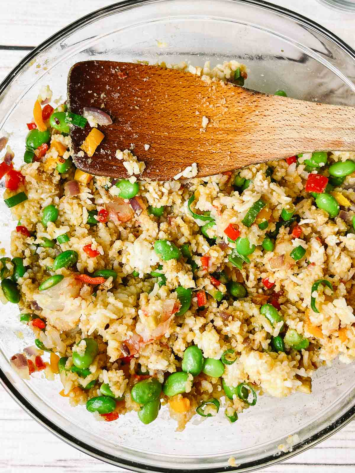 a large glass mixing bowl filled with a fried rice mixture and a wooden spatula
