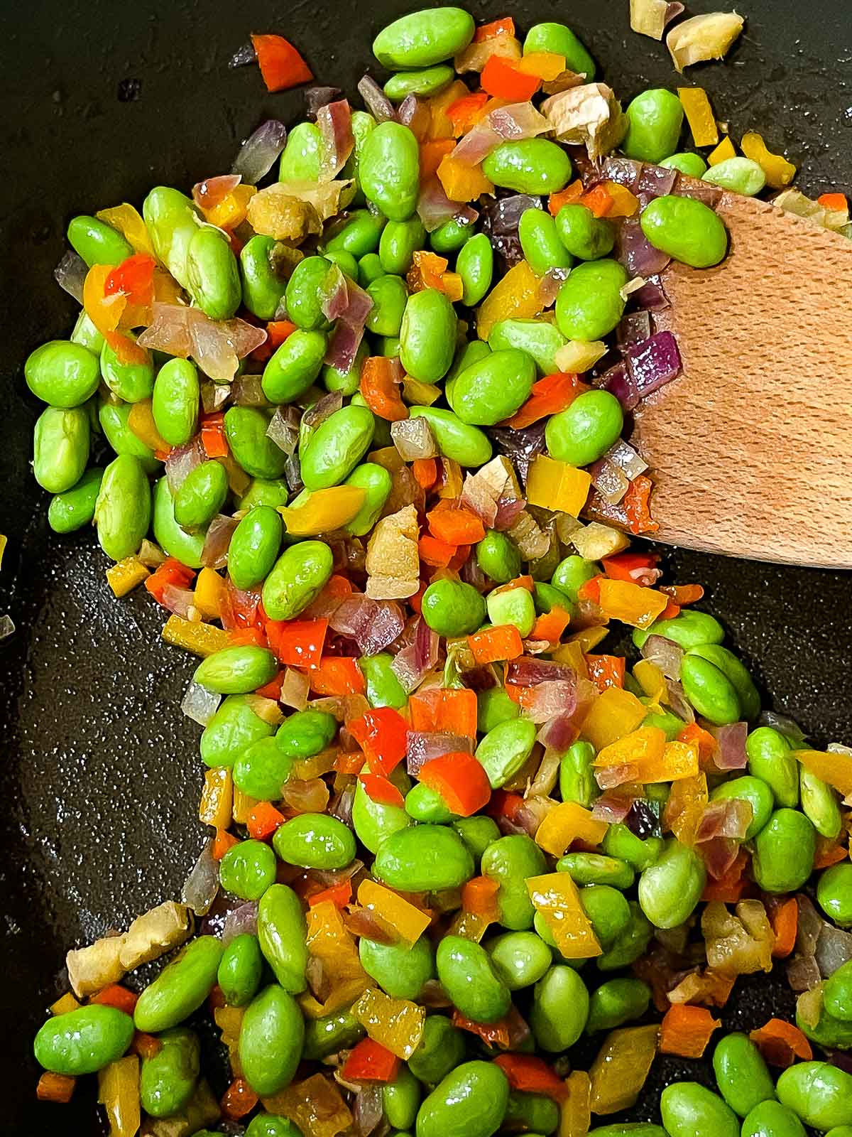 colorful veggies being stir-fried with a wooden spatula