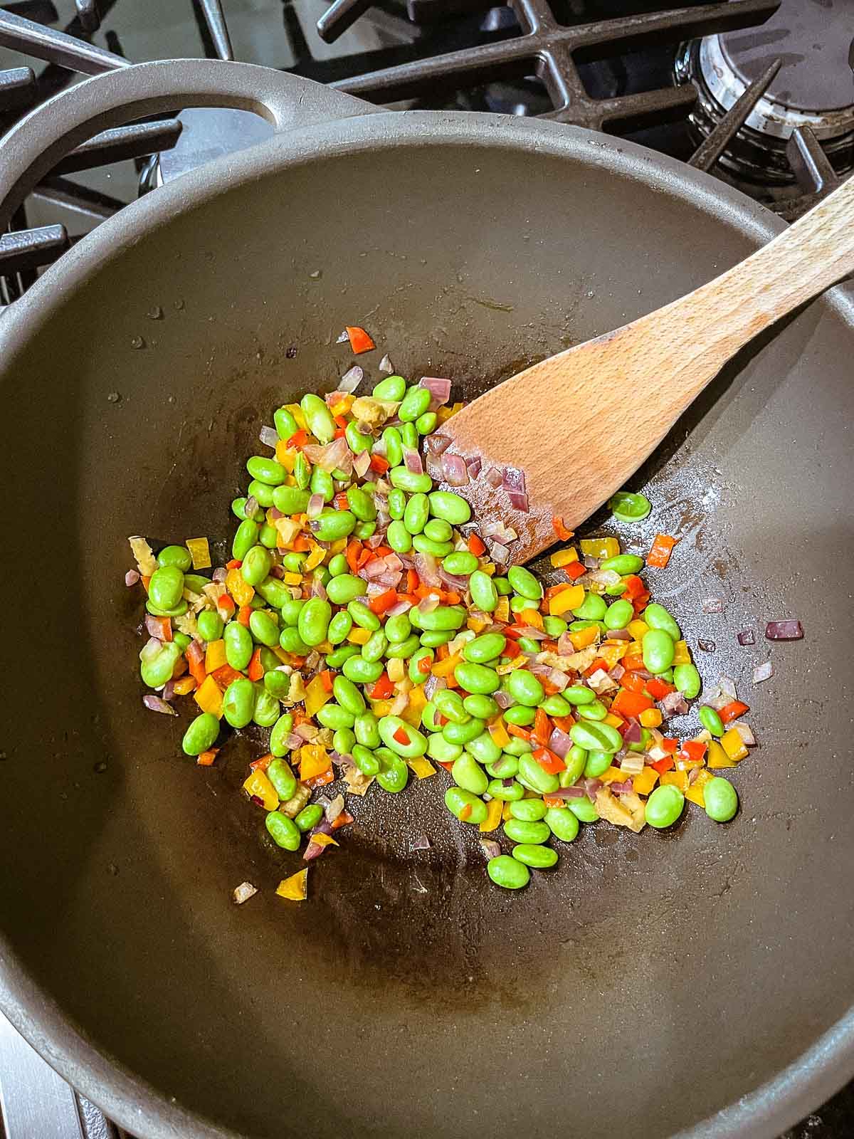 colorful veggies being stir-fried in a large wok with a wooden spatula over the stove