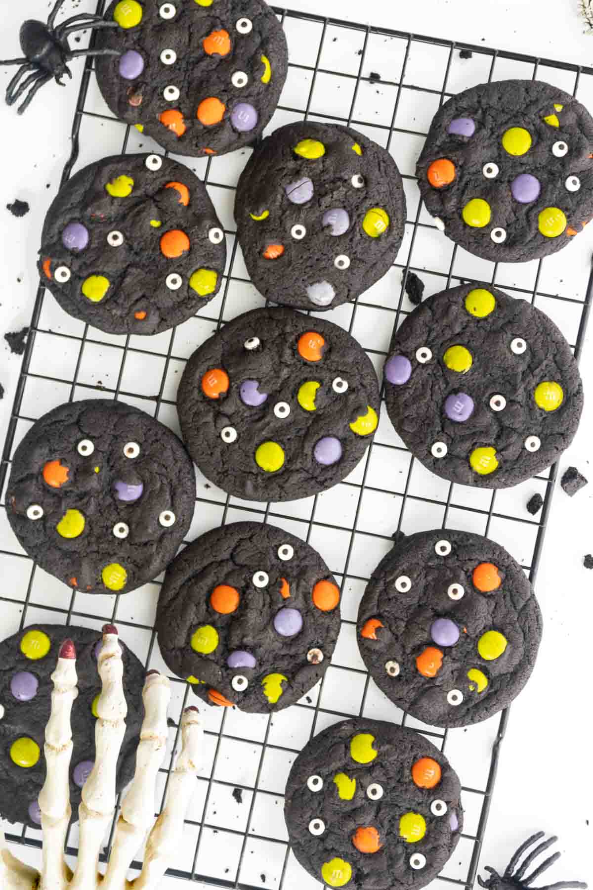 black cocoa Halloween cookies topped with colorful M&M's and candy eyeballs on a baking rack.