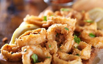 Fried and crispy calamari rings on a wooden board with lemon wedges on the side.