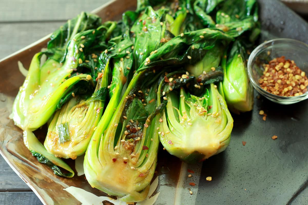 Halved baby bok choy that's been seared and topped with red pepper flakes on top of a gray serving platter.