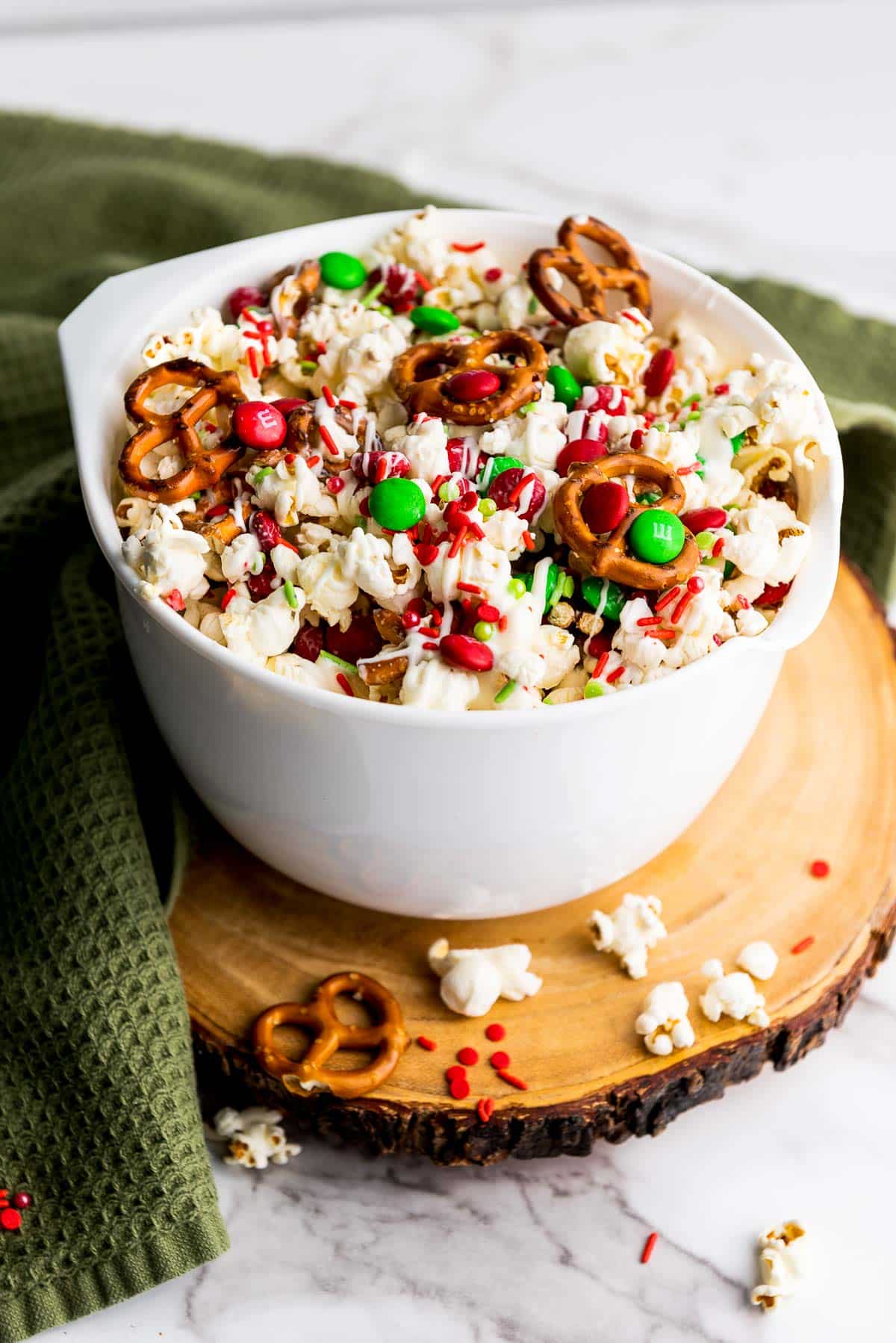 Christmas popcorn Santa munch in a white bowl on top of a round wooden board on a marble surface with a green napkin on the side.