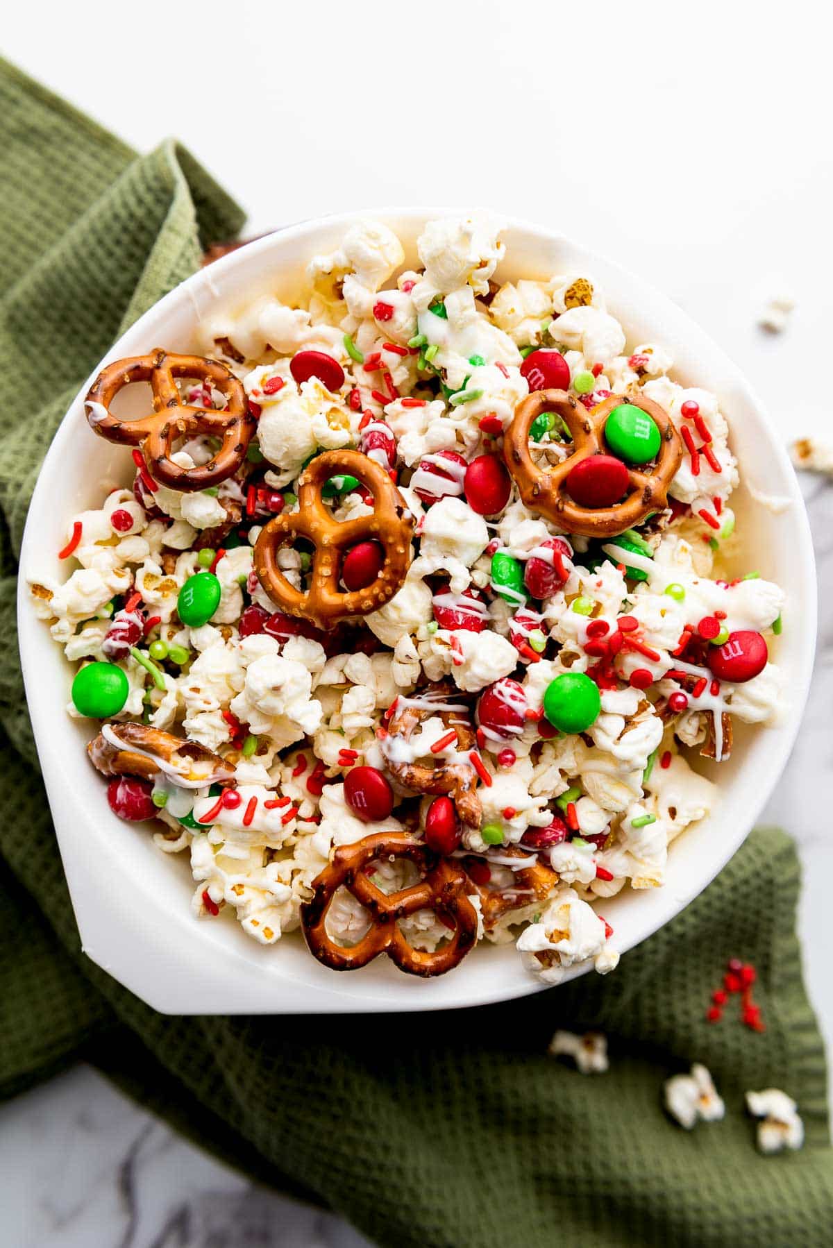 Christmas popcorn Santa munch in a white bowl on top of a round wooden board on a marble surface with a green napkin on the side.