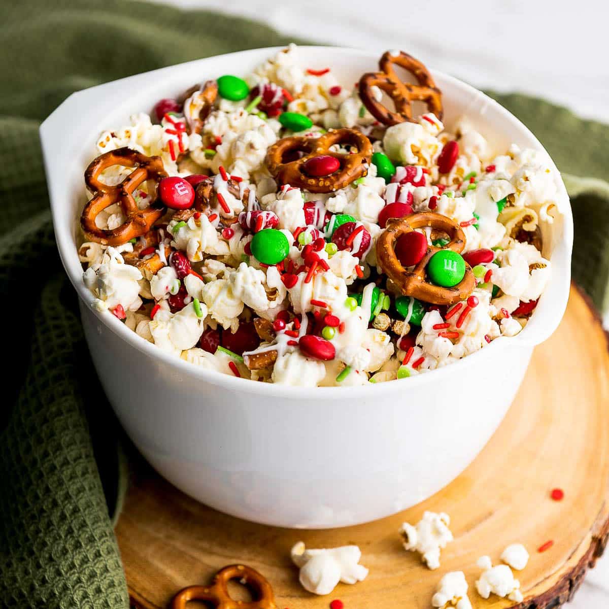 Christmas popcorn Santa munch in a white bowl on top of a round wooden board with a green napkin on the side.
