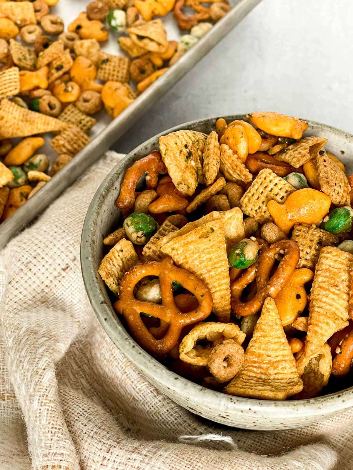 A bowl of Furikake chex mix with a linen napkin on the side and a baking tray in the background.