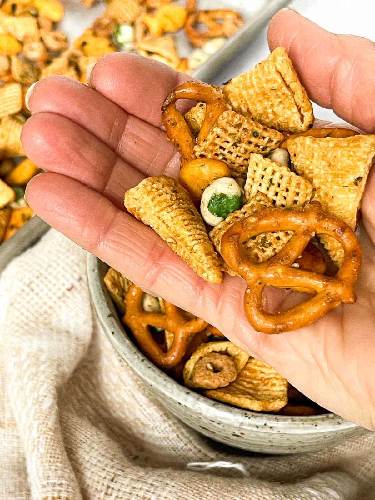 A hand holding Furikake Chex Mix above a bowl of Chex mix and a napkin.