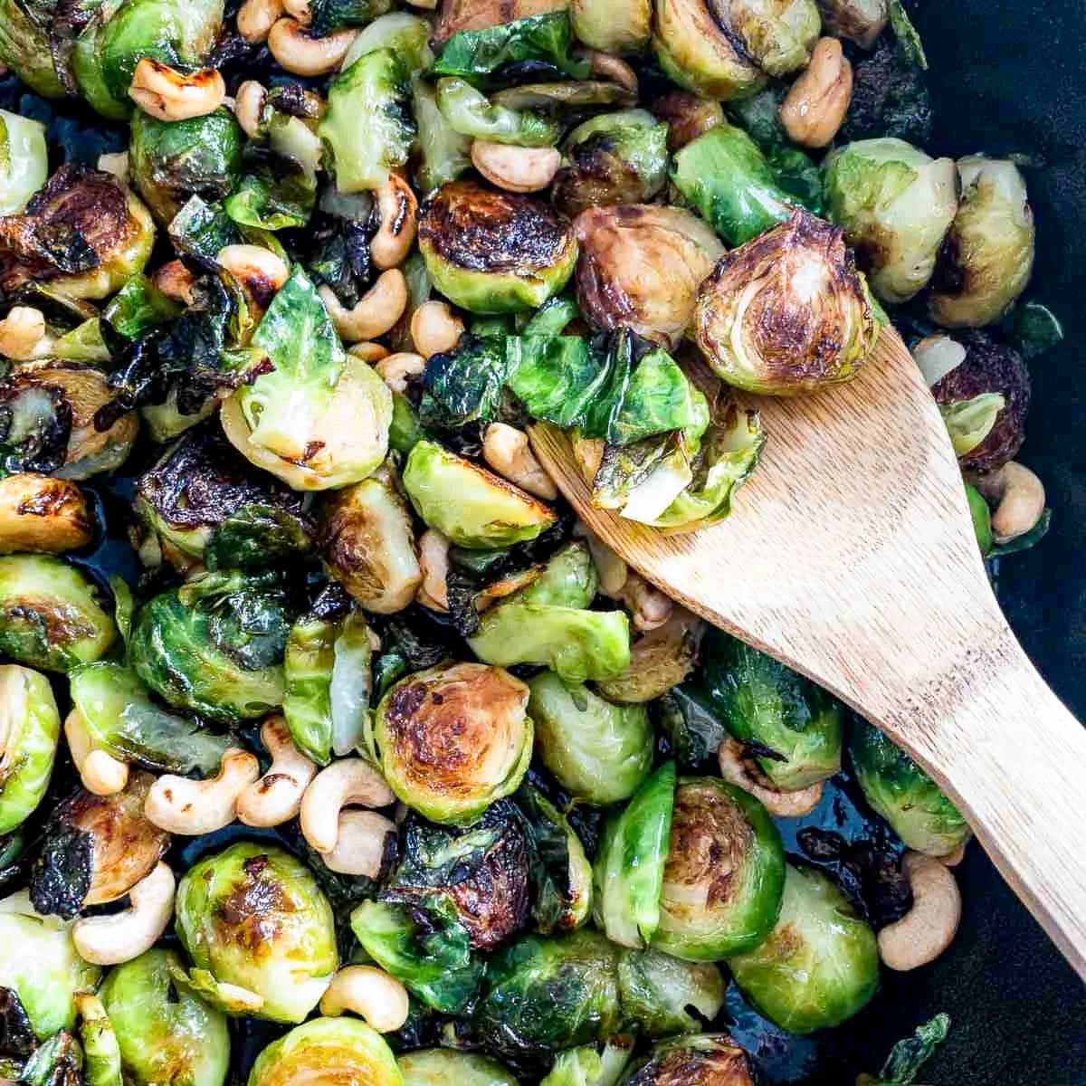 Freshly roasted Brussels sprouts holiday side dish tossed in a sriracha sauce with a wooden spoon.